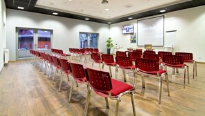 A conference room with rows of red chairs, a projector screen, and a large window with a view of buildings. - Dolina Leśnicy SKI & SPA Resort (Brenna)