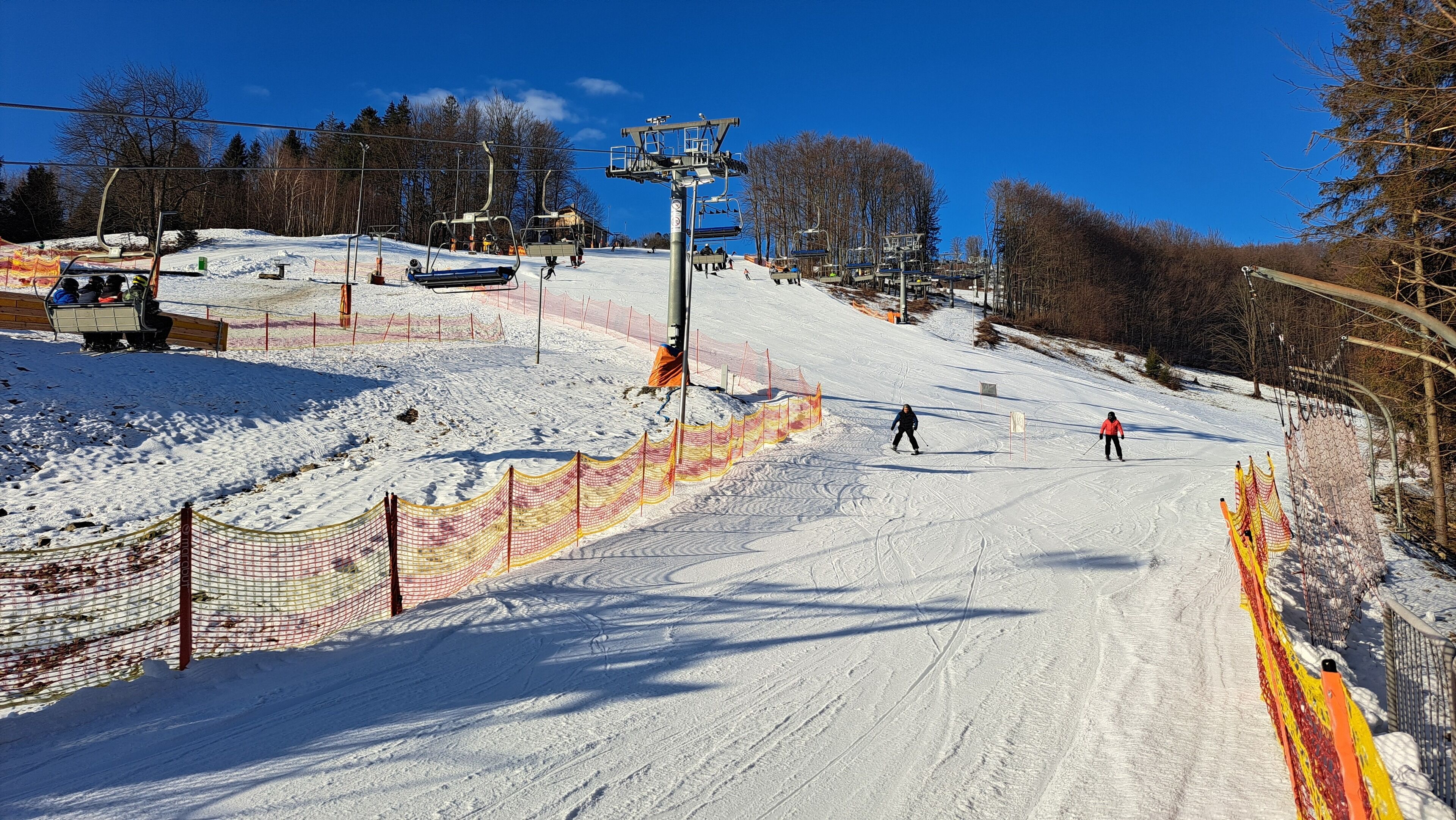 A ski slope with a chairlift, snow fences, and skiers.