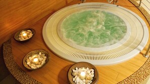 A hot tub surrounded by wooden flooring, with three bowls of pebbles and candles. - Dolina Leśnicy SKI & SPA Resort (Brenna)