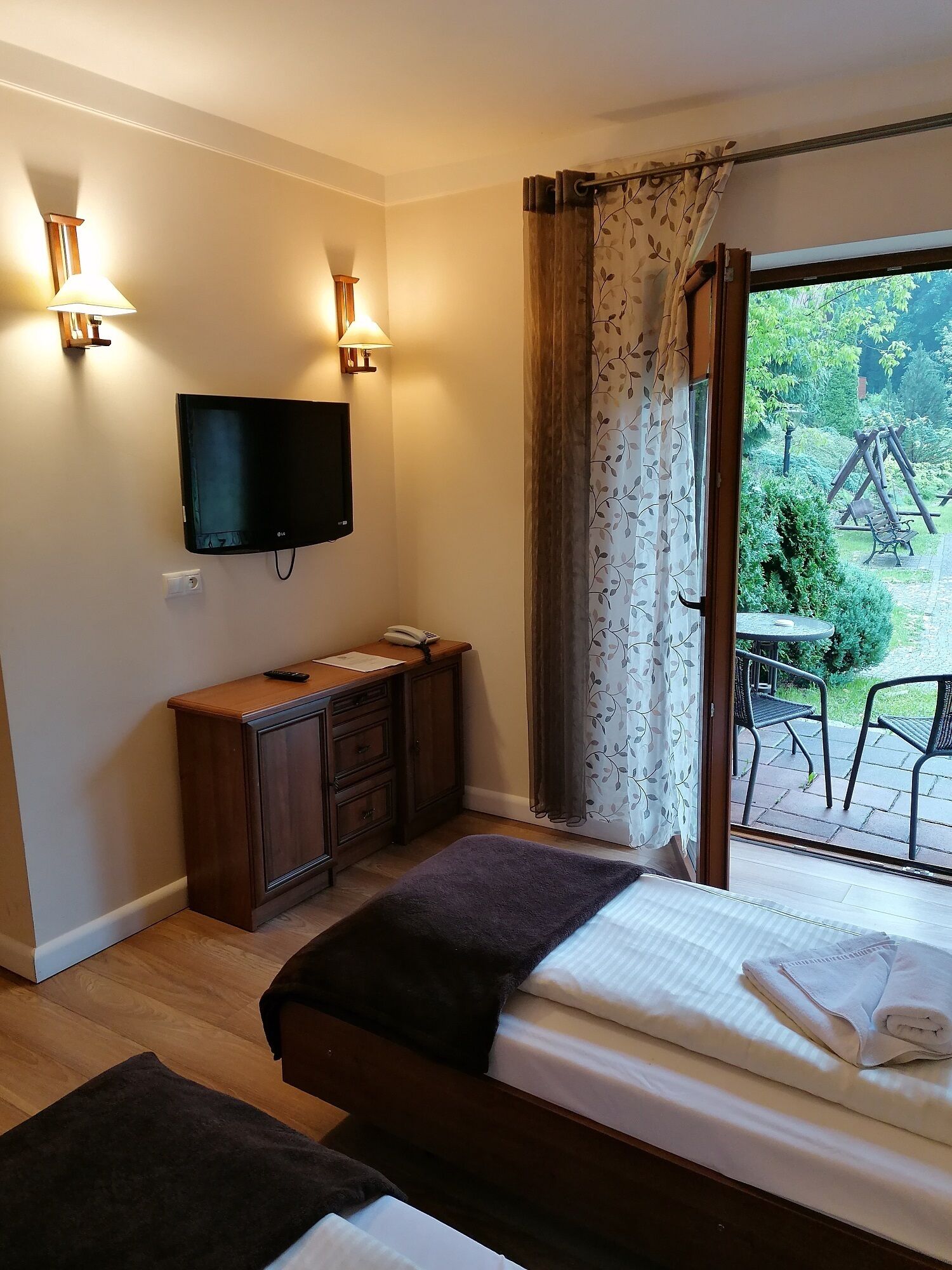 Un dormitorio con cama, escritorio, televisor y vista a un jardín a través de una ventana.