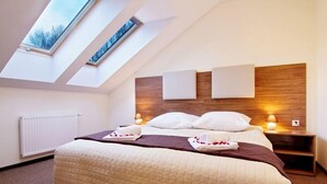 A modern hotel room with a sloped ceiling, skylights, a large bed with a quilted duvet, two bedside lamps, and a wooden headboard. - Dolina Leśnicy SKI & SPA Resort (Brenna)