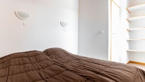 Een slaapkamer met een bruin gewatteerd beddegoed, witte muren en een houten deur.