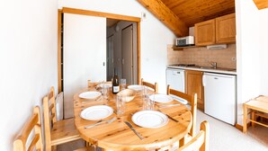 Een houten eettafel gedekt met borden, bestek en glazen in een keuken met houten kasten en apparatuur.