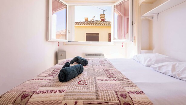Une chambre à coucher avec un lit, une fenêtre donnant sur des immeubles et un radiateur.