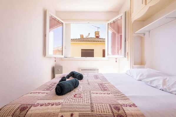 Un dormitorio con cama, ventana y vistas a edificios, además de un radiador.