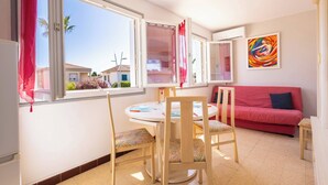 Une pièce comprenant une table à manger, des chaises, un canapé rouge, une fenêtre avec des rideaux et un tableau abstrait aux couleurs vives accroché au mur.