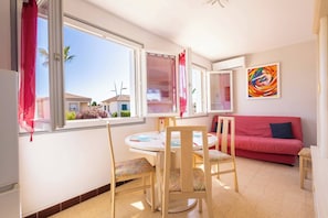 Una habitación con una mesa de comedor, sillas, un sofá rojo, una ventana con cortinas y un cuadro abstracto y colorido en la pared.