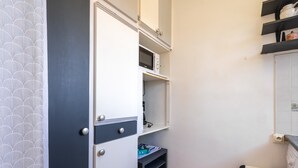 Une petite salle de bain équipée d’un micro-ondes encastré, d’une petite étagère et d’une poubelle.