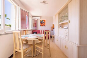 Un comedor con una mesa redonda, sillas, un armario con puertas de vidrio y un cuadro abstracto de colores en la pared.