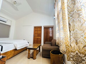 Ein Zimmer mit einem Bett, einem Holztisch, einer Couch und einem gemusterten Vorhang.