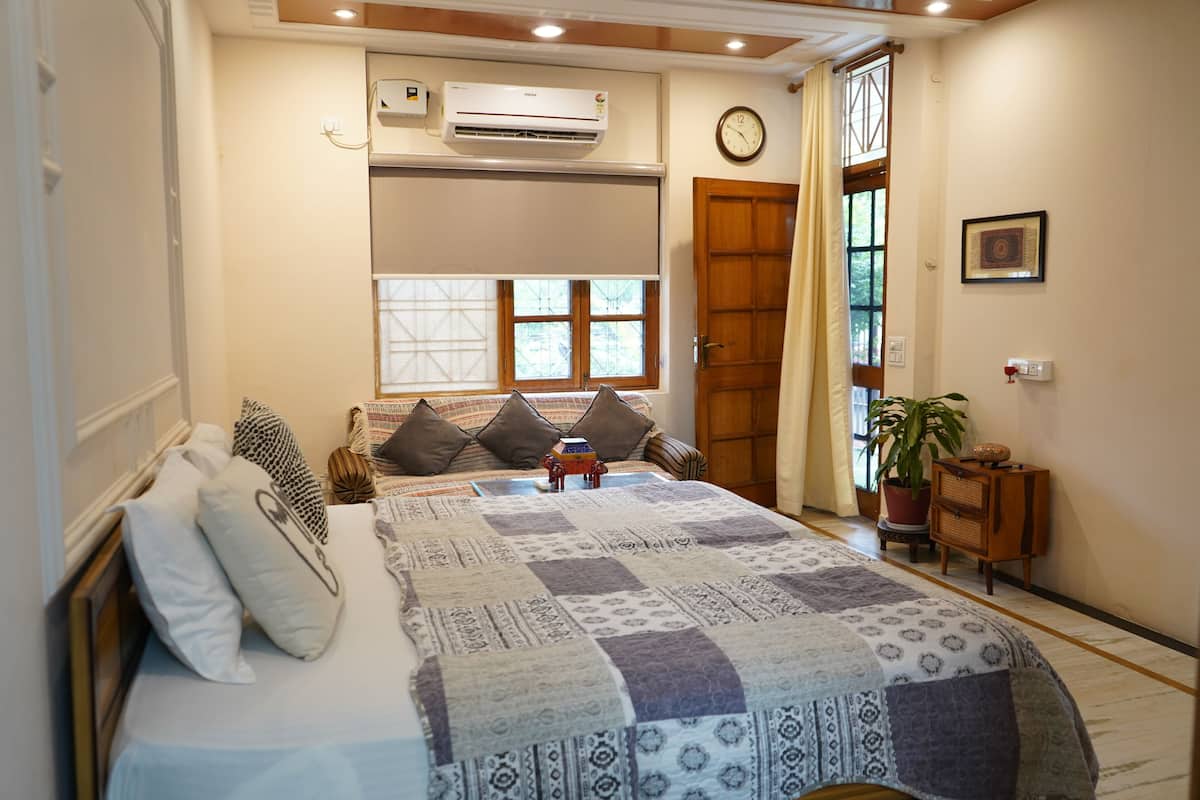A bedroom with a bed, pillows, a window, an air conditioner, a clock, and a door.