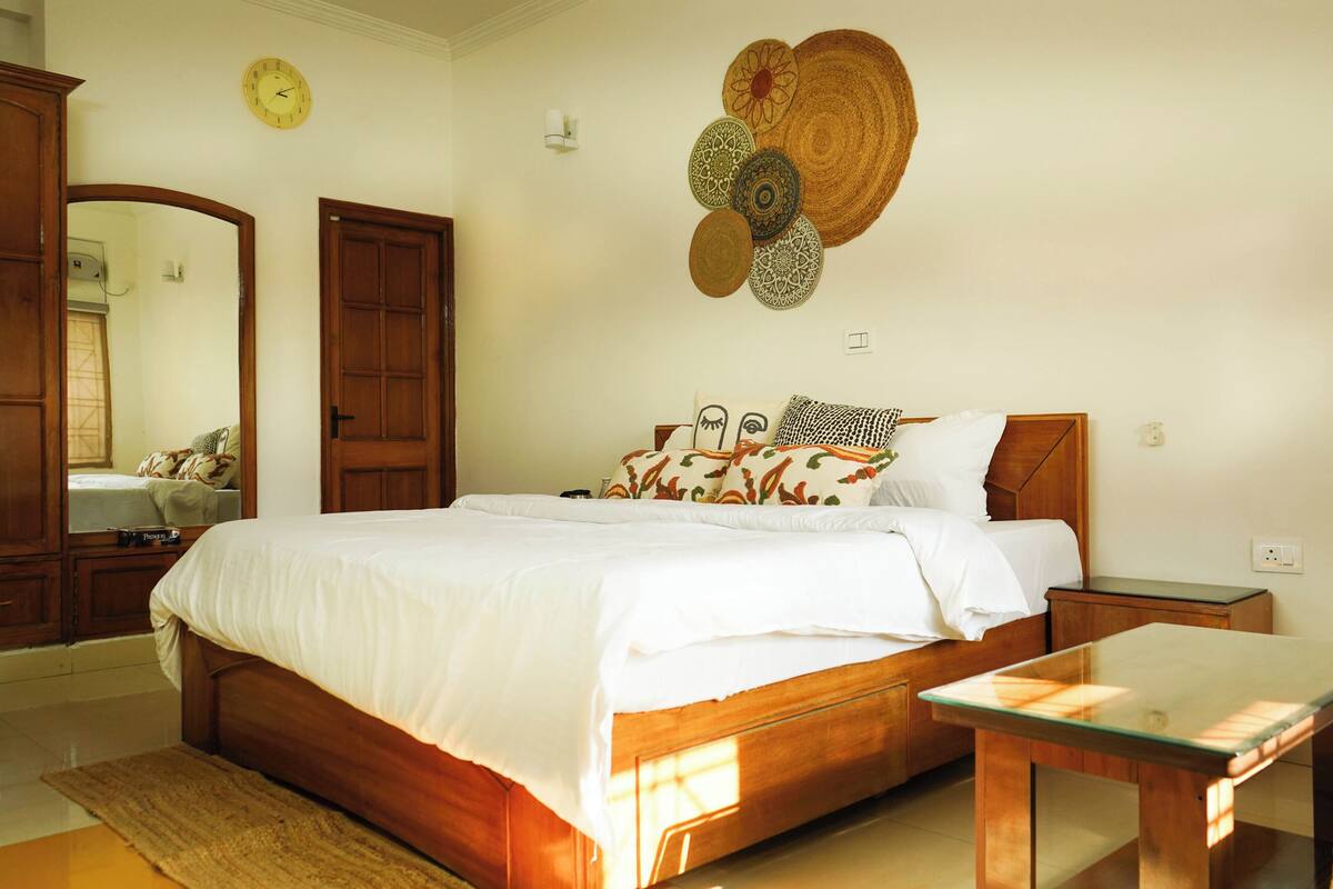 A bedroom with a wooden bed, a bedside table, a mirror, and a wall clock.