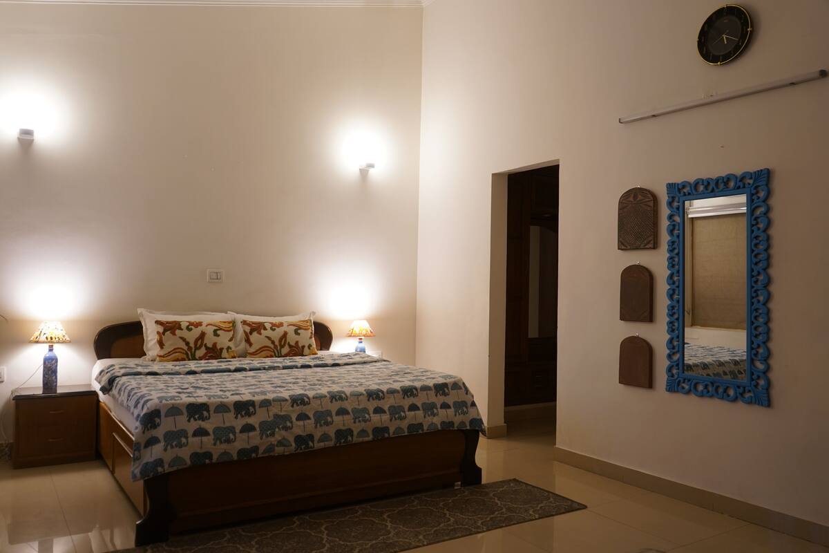 A bedroom with a bed, two bedside lamps, a wall clock, and a mirror with decorative frames.