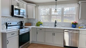 A modern kitchen with white cabinetry, stainless steel appliances, a microwave, and a dishwasher. - The Majestic View / Luxury Stay Gulf Course Views / 4-Bedroom House (Bloomfield)