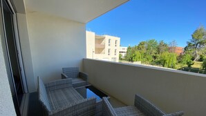 A balcony with wicker furniture and a clear view of buildings and trees. - Modern Apartment with Parking in Argelès-sur-Mer (Argelès-sur-Mer)