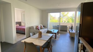 A modern living room with a sofa, a dining table, and a TV. There is a balcony with a view of trees and buildings. - Modern Apartment with Parking in Argelès-sur-Mer (Argelès-sur-Mer)