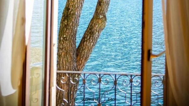 Vista attraverso una finestra con ringhiera metallica, su un'area d'acqua e un paesaggio montuoso.