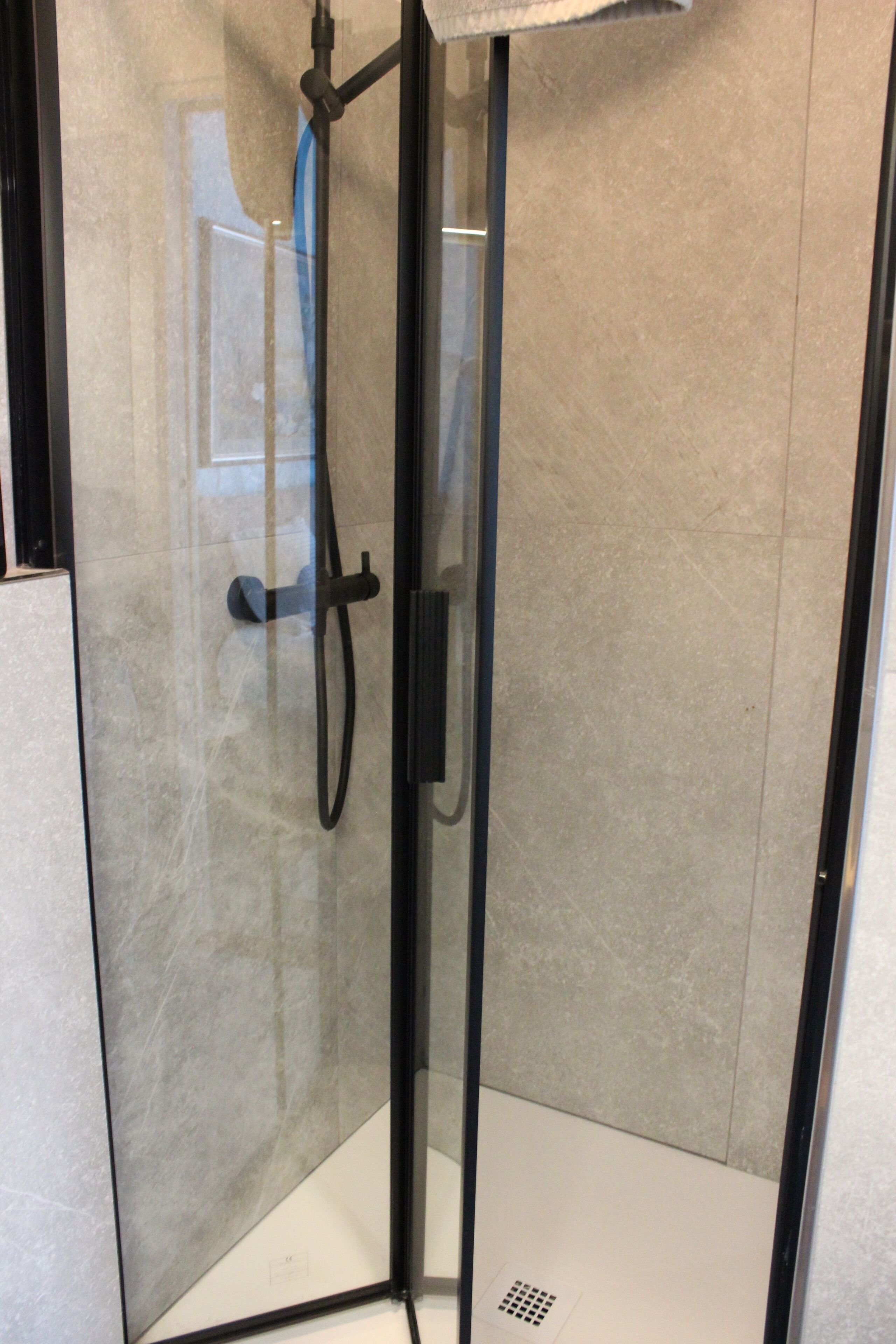 A glass-enclosed shower stall with a handheld showerhead and a control panel.