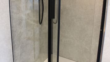 A glass-enclosed shower stall with a handheld showerhead and a control panel.