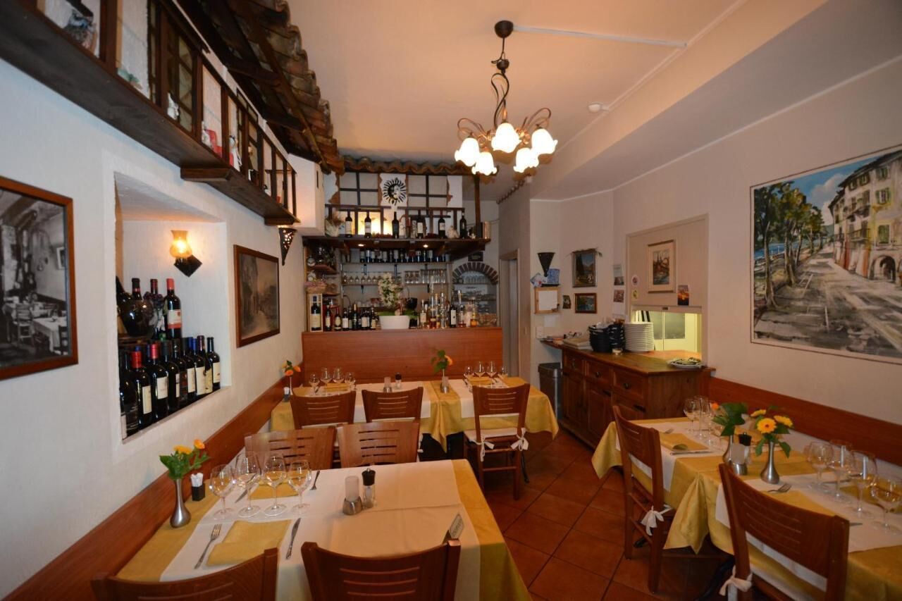 A restaurant with multiple dining tables, a bar area with shelves of bottles, and a painting on the wall.