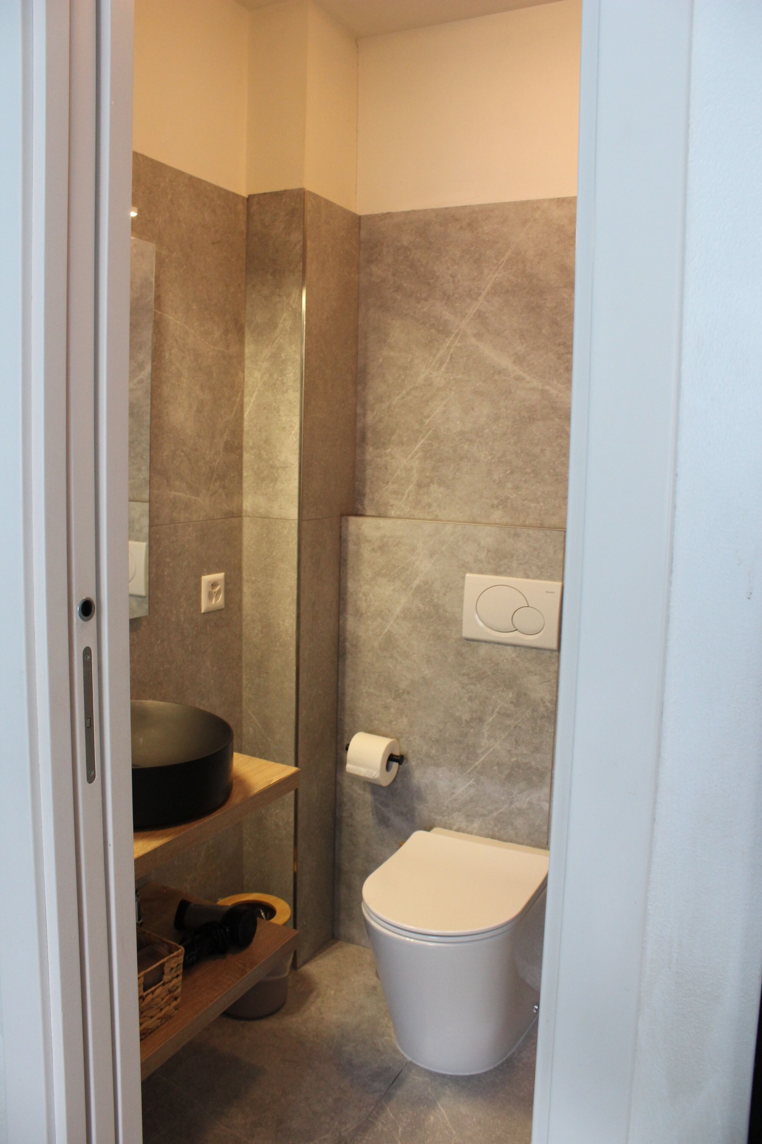 Un bagno compatto con il water, un lavandino e uno scaffale con un cesto.