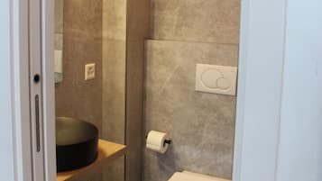 Un bagno compatto con il water, un lavandino e uno scaffale con un cesto.