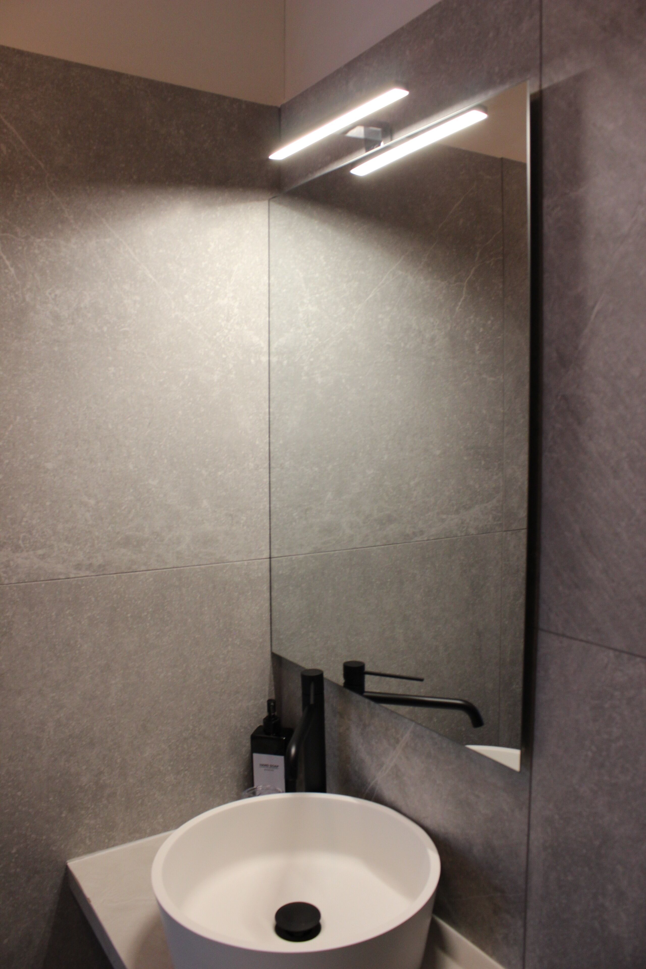 A modern bathroom with a white sink, a mirror, and a light fixture.