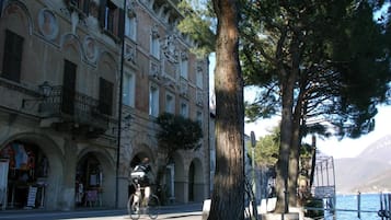 Rua com um ciclista, uma árvore e um edifício com janelas em arco e varandas.