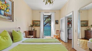Una camera da letto con un letto, cuscini verdi, una scrivania e vista sul mare attraverso una porta.
