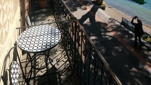 Un balcone con tavolo e sedie decorate, con vista su un sentiero lungo il lago, alberi e una barca.