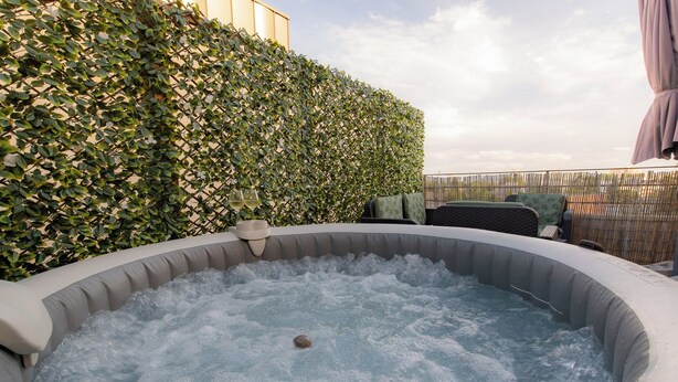 A hot tub surrounded by a hedge, with a wooden fence and outdoor furniture in the background. - LE PETIT SESAME L' évasions cosy jacuzzi terrace wifi parking 2 steps stadiumDF (Saint-Denis)