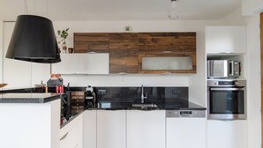A modern kitchen with white cabinetry, a black countertop, a built-in microwave, and an oven. - LE PETIT SESAME L' évasions cosy jacuzzi terrace wifi parking 2 steps stadiumDF (Saint-Denis)