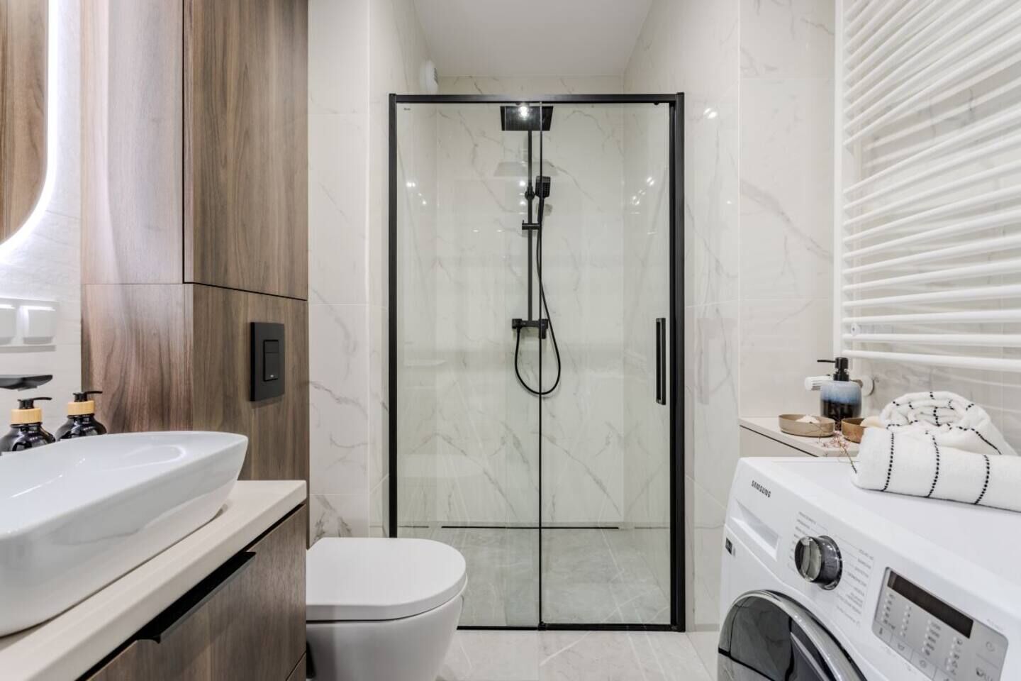 Un baño moderno con ducha de vidrio, inodoro, lavamanos y lavadora.
