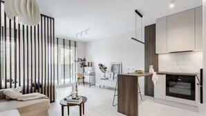 Ett modernt kök med en inbyggd ugn, en matplats med bord och stolar samt ett vardagsrum med en soffa och en dekorativ lampa.