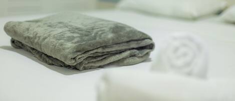 A neatly made bed with a folded blanket and a rolled towel.