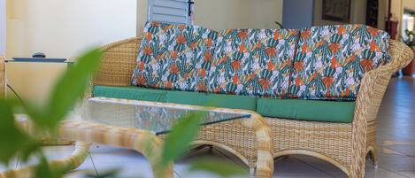 Un sofá de mimbre con un cojín estampado en una habitación luminosa con suelo de baldosas.