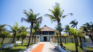 A building with a tiled roof, surrounded by palm trees and white fences. - Rota do Sol Praia Hotel (Guaratuba)