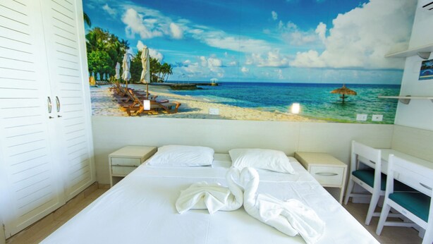 A hotel room with a bed, a small bedside table, a chair, and a large beach mural on the wall. - Rota do Sol Praia Hotel (Guaratuba)