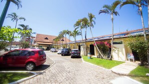 A street view with parked cars, palm trees, and a building with a tiled roof. - Rota do Sol Praia Hotel (Guaratuba)