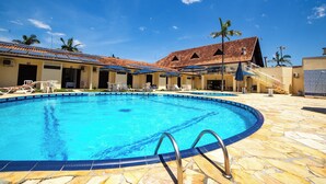A swimming pool with lounge chairs and umbrellas, surrounded by buildings with tiled roofs and palm trees. - Rota do Sol Praia Hotel (Guaratuba)