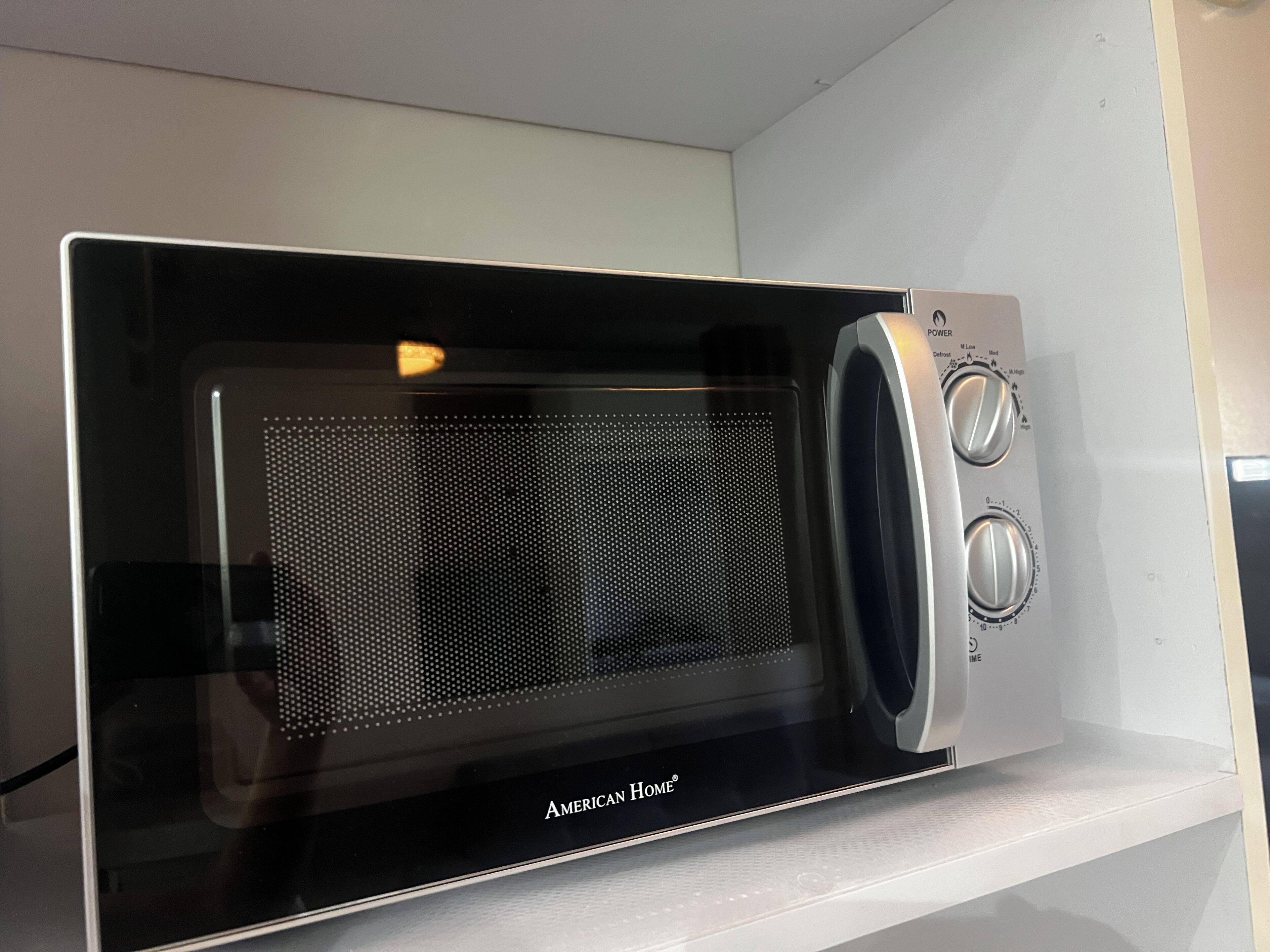 Un forno a microonde con display digitale e manopole di controllo, posizionato su uno scaffale bianco.