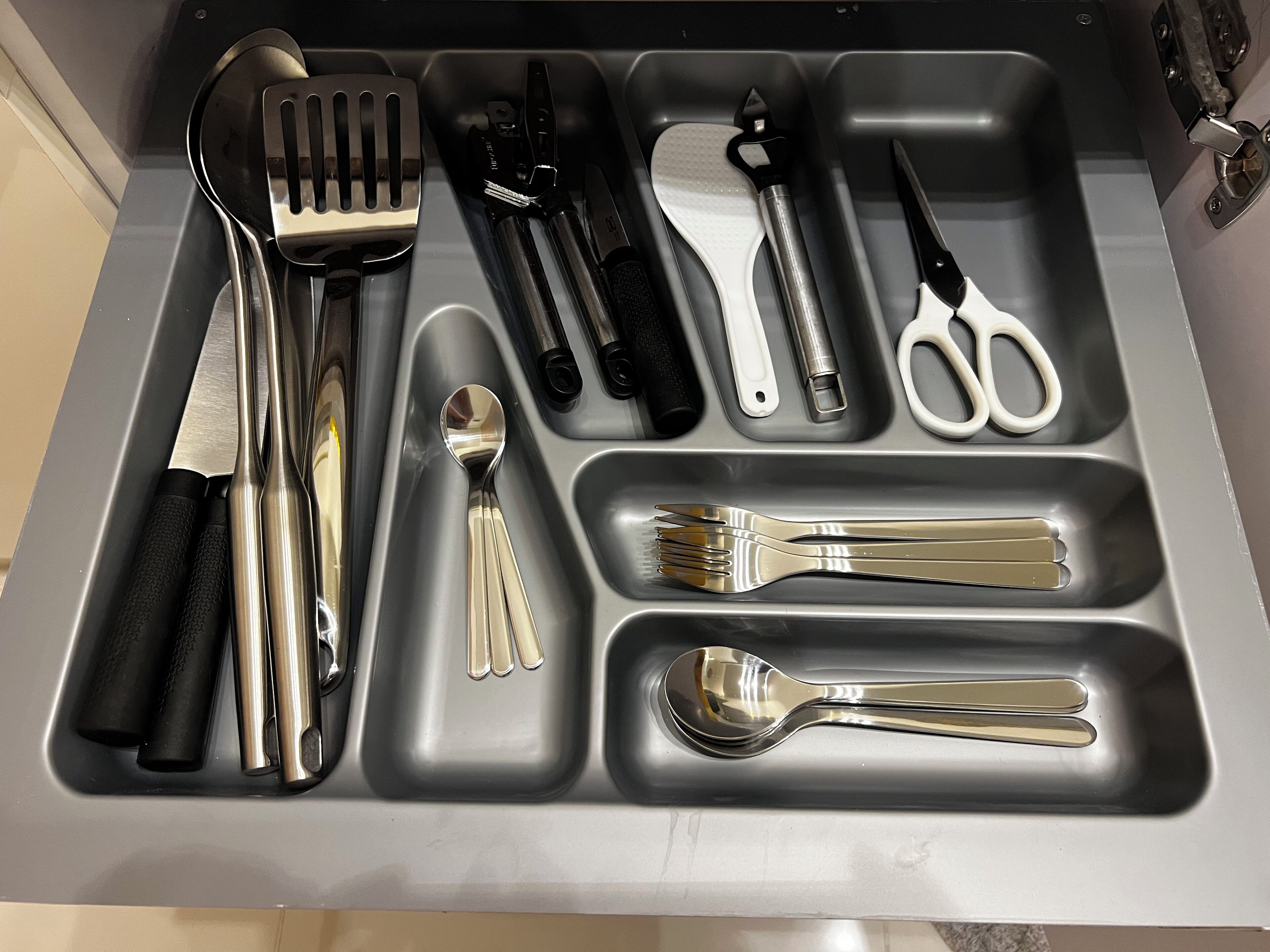 A kitchen drawer with various utensils organized in compartments.