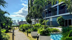 Un camino conduce a una piscina rodeada de exuberante vegetación y un edificio moderno con balcones.