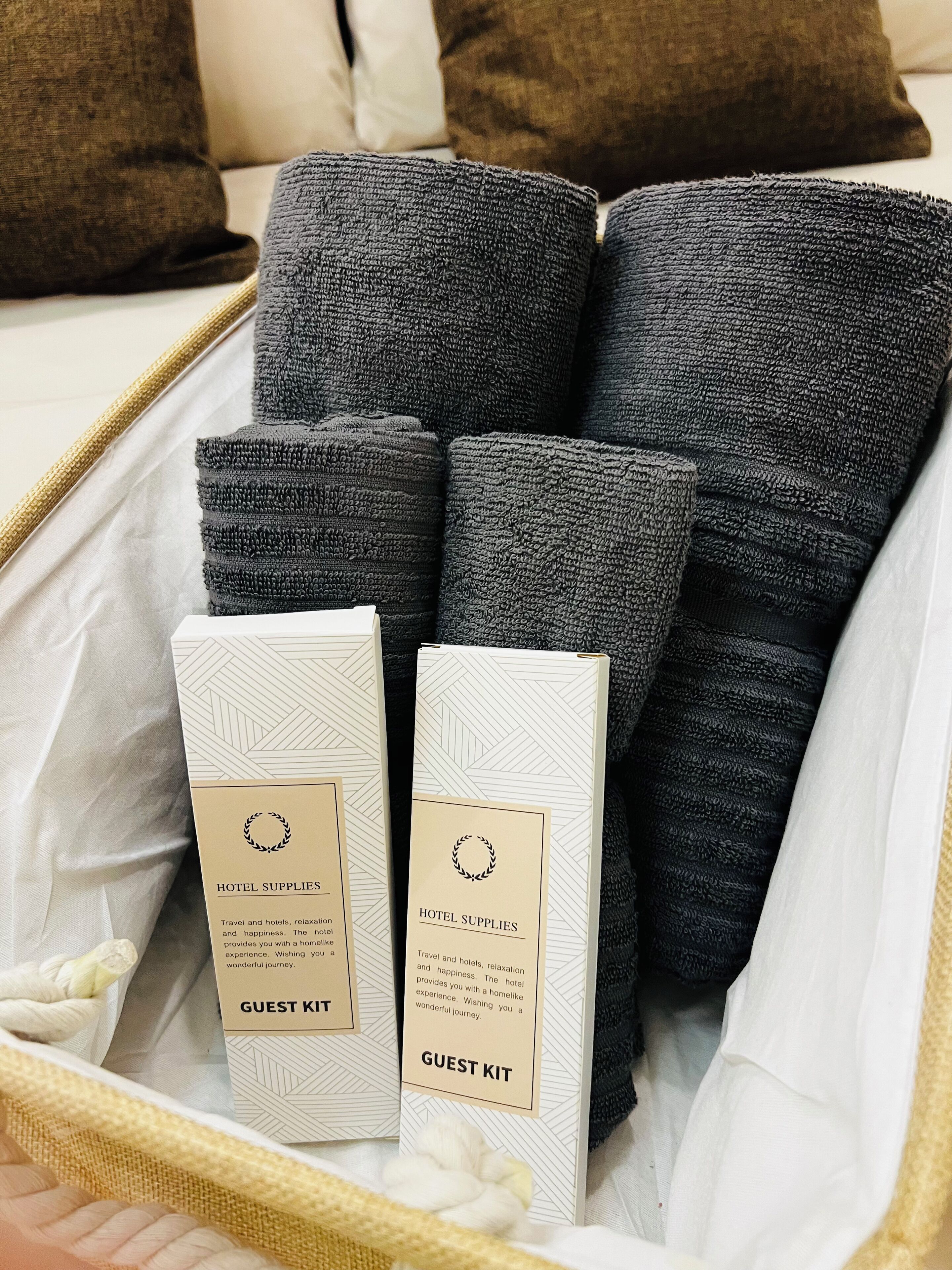 Ein Gästepaket mit einer Hotelbroschüre und mehreren grauen Decken in einem gewebten Korb.
