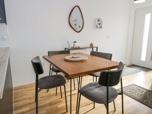 A dining area with a wooden table, four chairs, a mirror, a small shelf with decorative items, and a radiator. - Tay View (Aberfeldy)