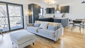 Un salon moderne avec un canapé gris, un pouf et un coin repas comprenant une table et des chaises.