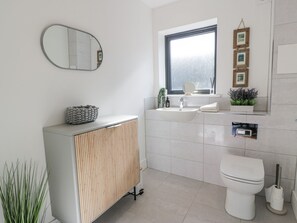 A modern bathroom with a toilet, sink, and mirror. There is a window above the sink and a small plant on the windowsill. - Tay View (Aberfeldy)