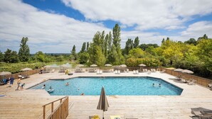 Ein rechteckiger Pool mit umlaufender Holzterrasse, Liegestühlen und Sonnenschirmen.