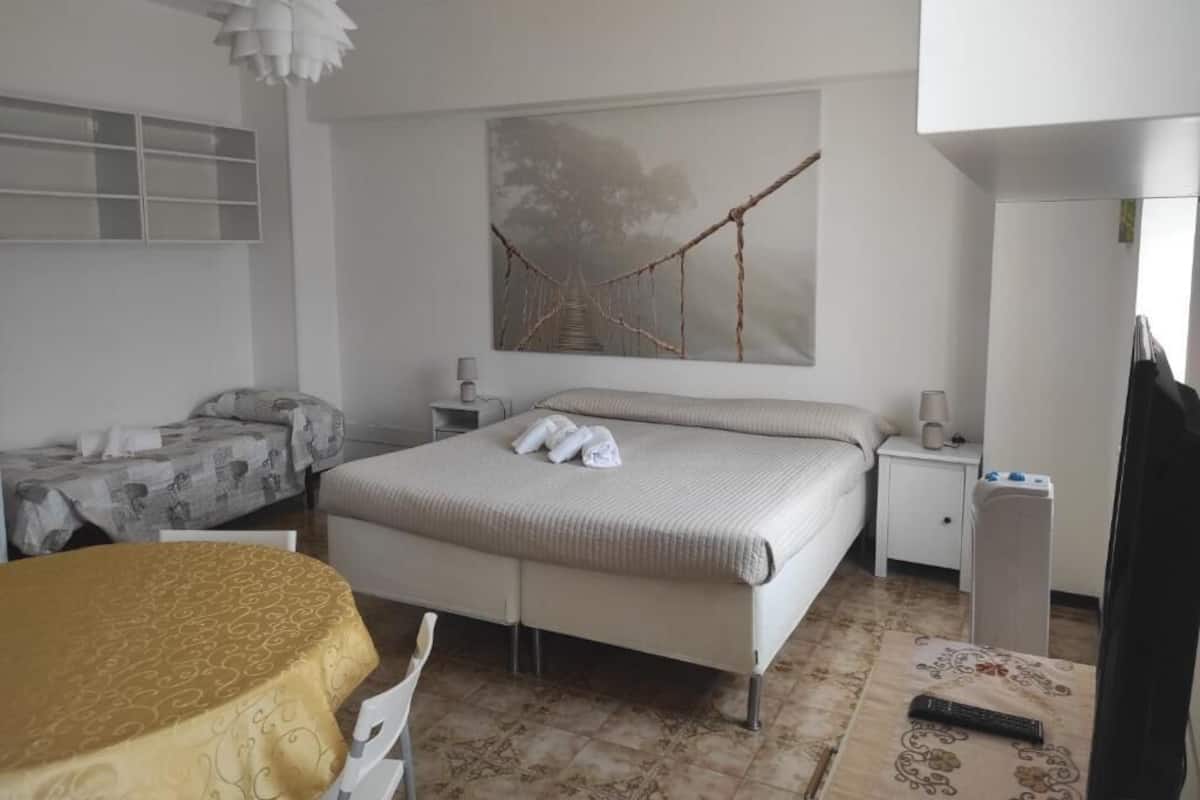 Una camera da letto con un letto, un comodino, una sedia, un tavolo con tovaglia, una lampada a sospensione e un'opera d'arte appesa al muro.
