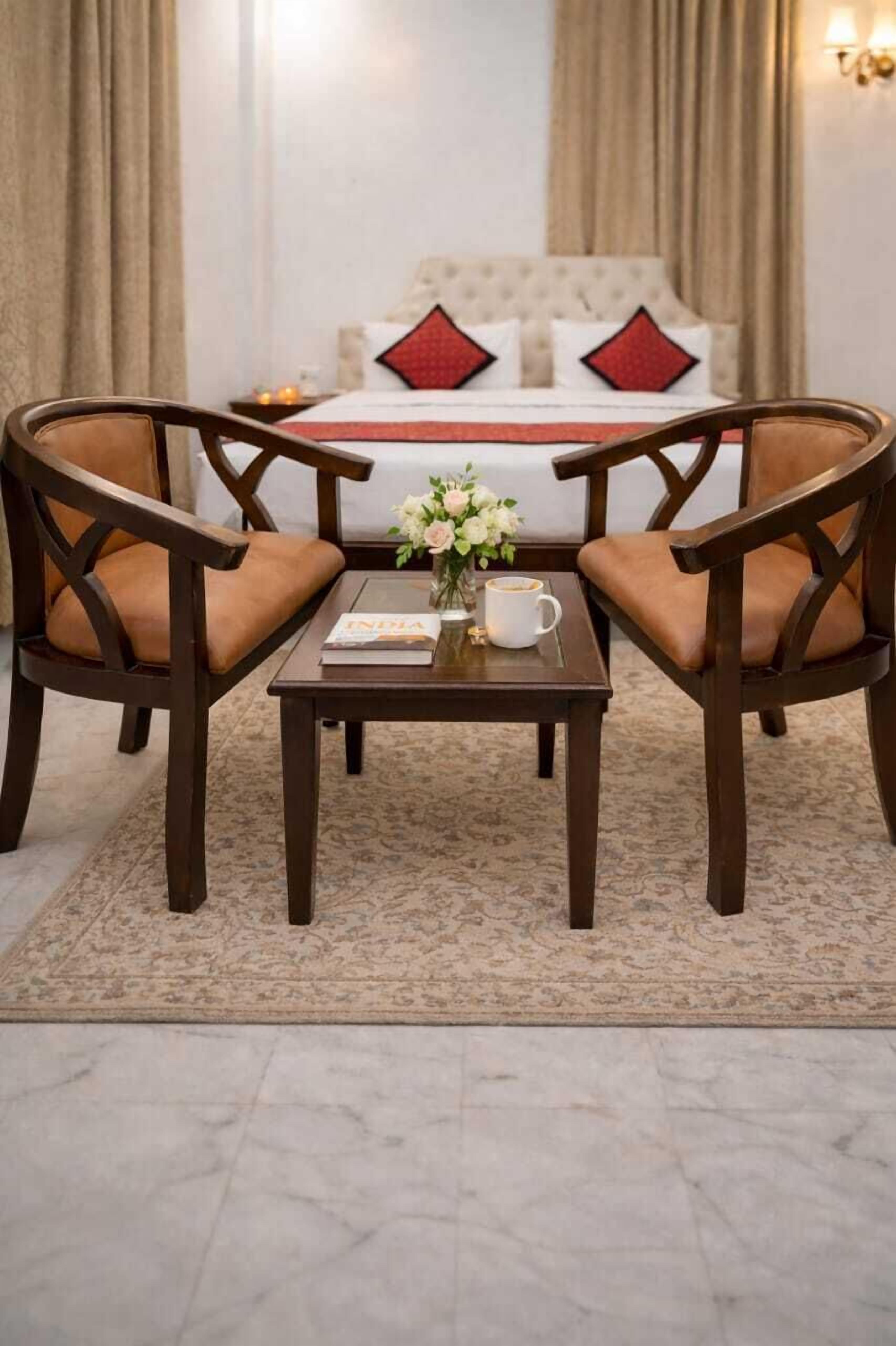 A hotel room with a bed, two armchairs, a coffee table with a book and flowers, and a nightstand with a lamp.
